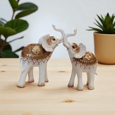 Decorative elephant figurines with intricate designs on a wooden surface with plants in the background.