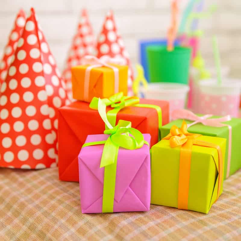 Brightly wrapped colorful gift boxes with ribbons, surrounded by red polka-dotted party hats and festive table setup, perfect for celebrations and gifting by Motumal Giftwala.
