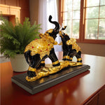 Decorative black and gold elephant statue on a wooden surface with a plant in the background.