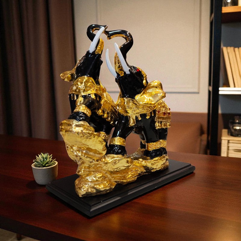 Decorative sculpture of three figures on a black base with gold accents, placed on a wooden surface.