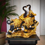 Decorative gold and black elephant statue on a stand with a plant in the background.