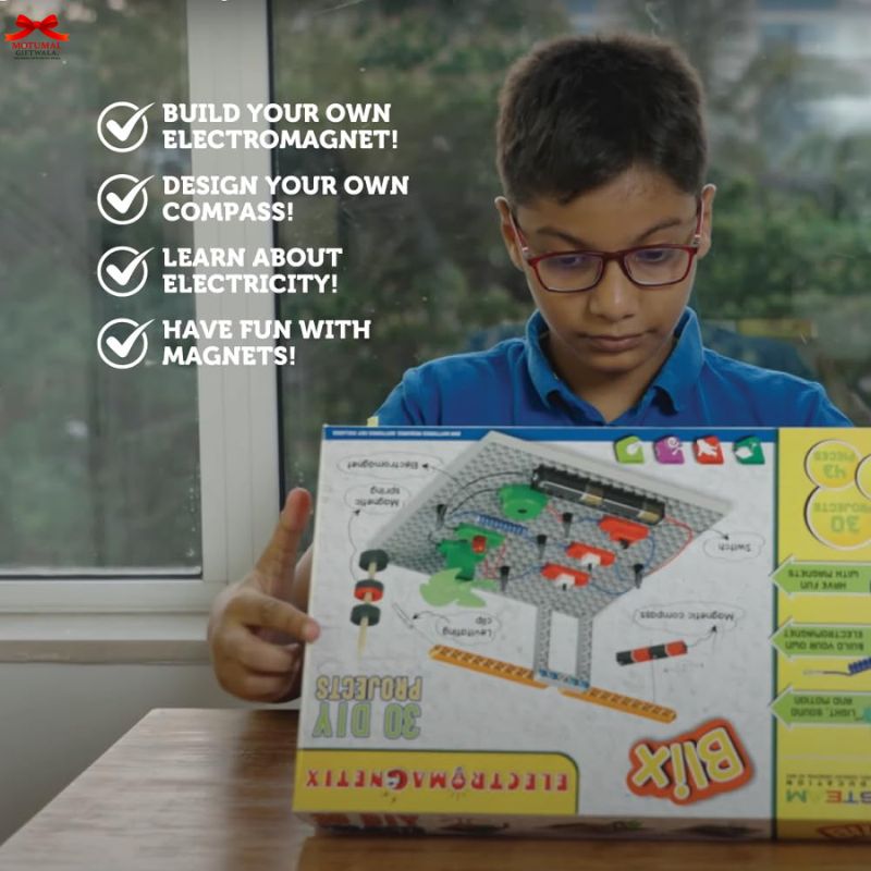 Child holding a science kit box with educational text about magnets and electricity.
