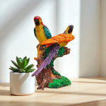 Colorful parrot figurine on a branch with a small plant on a wooden surface