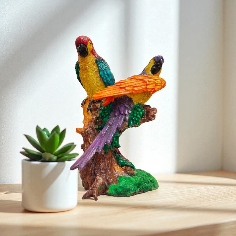 Colorful parrot figurine on a branch with a small plant on a wooden surface