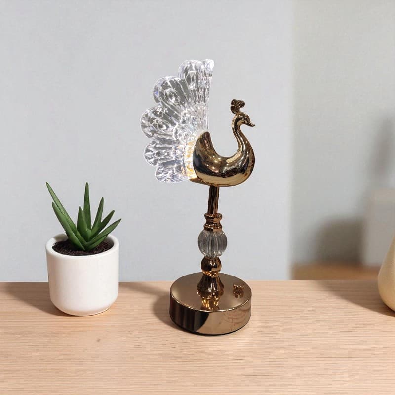 Decorative peacock sculpture on a wooden surface with a potted plant in the background