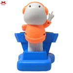 Toy figure with orange outfit and white face on a blue stand, with a visible brand logo in the corner.
