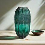 Green textured vase on a wooden surface with a soft light background
