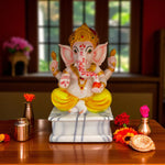 Front view of white ganesha idol seated on marble base with diya