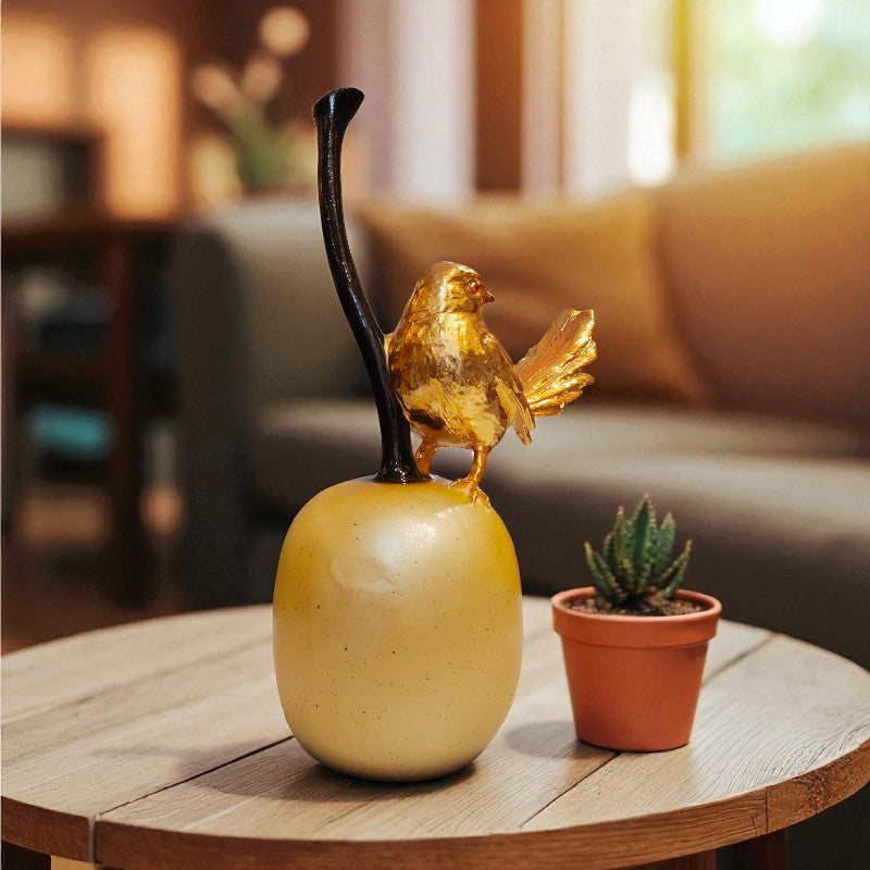 Decorative apple with a gold bird on top on a wooden table.