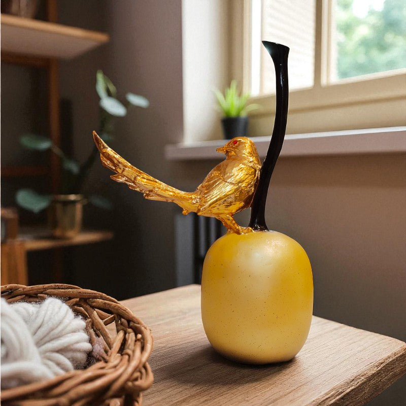 Decorative object with a gold bird on top of a yellow apple on a wooden surface.
