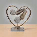 Decorative sculpture with heart frame, feathers, and glass balls on a wooden surface.