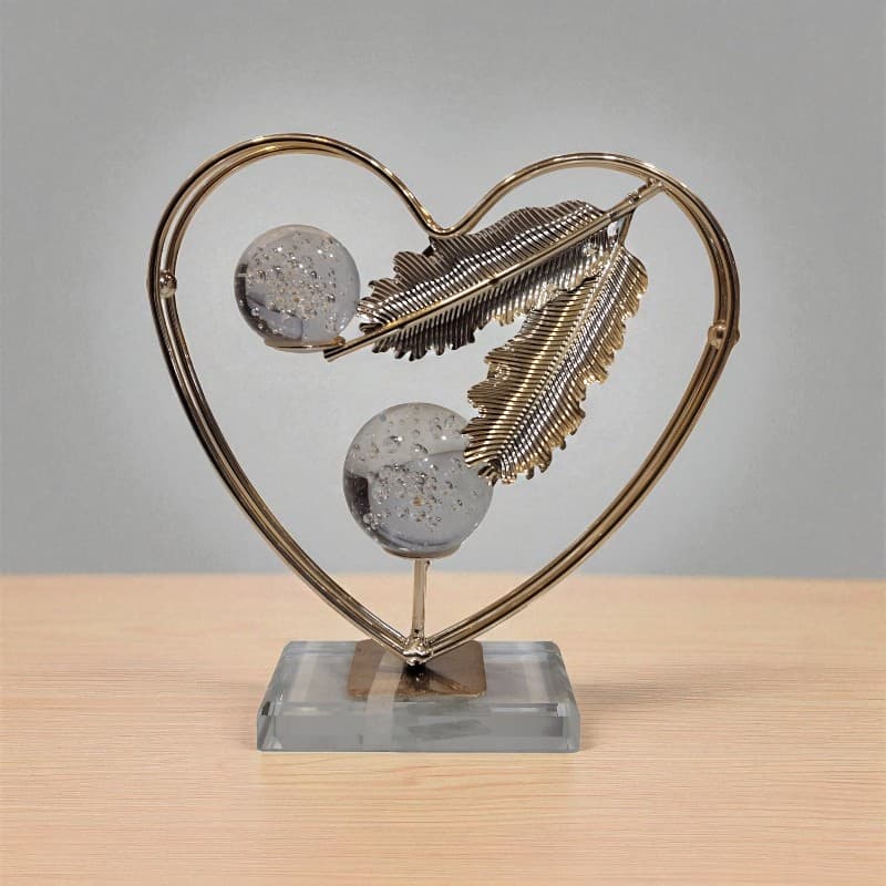 Decorative sculpture with heart frame, feathers, and glass balls on a wooden surface.