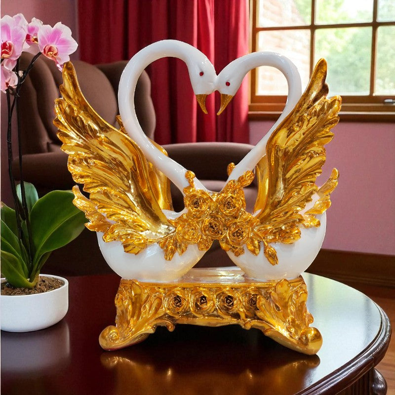 Decorative swan figurine with gold wings on a table with a pink curtain and plant in the background