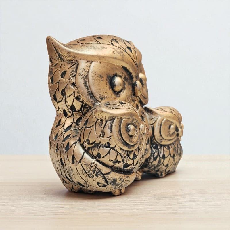 Bronze owl figurine on a light wooden surface with a plain background