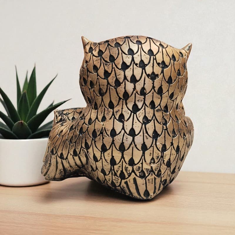 Decorative owl sculpture with a pattern on a wooden surface next to a plant.