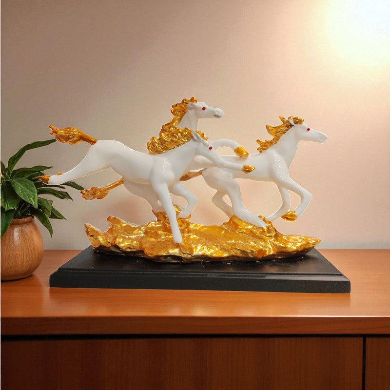 Decorative sculpture of three white horses with gold accents on a black base, placed on a wooden surface.