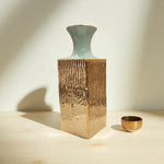 Ceramic vase on a wooden block with a small bowl on a neutral background