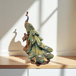Decorative peacock statue on a wooden surface with a neutral background