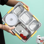 Stainless steel food container with yellow handles held by a person on a teal background