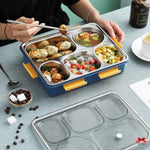 Person using a stainless steel bento box with compartments filled with food on a table.