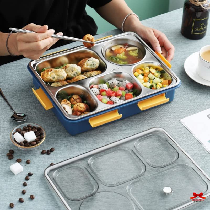 Person using a stainless steel bento box with compartments filled with food on a table.