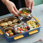 Person holding a small bowl of soup over a stainless steel bento box with compartments filled with food.