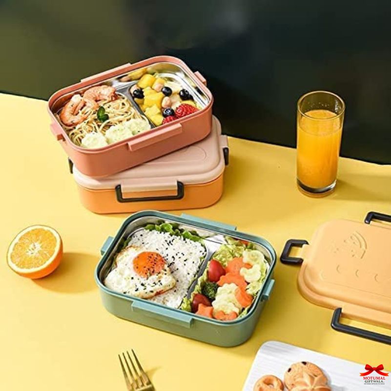 Two bento boxes with food on a yellow table, next to a glass of orange juice.