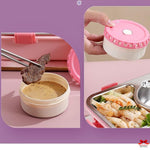 Pink and white food container with condiment, skewer, and pasta dish on a pink background
