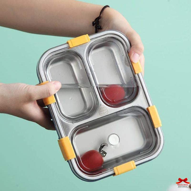 Stainless steel bento box with yellow accents held by a hand against a light blue background