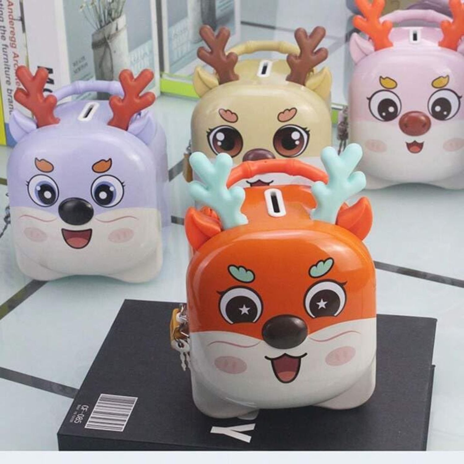 Assorted reindeer shaped metal piggy banks displayed against red background, adorable design with antlers and lock, by Motumal Giftwala