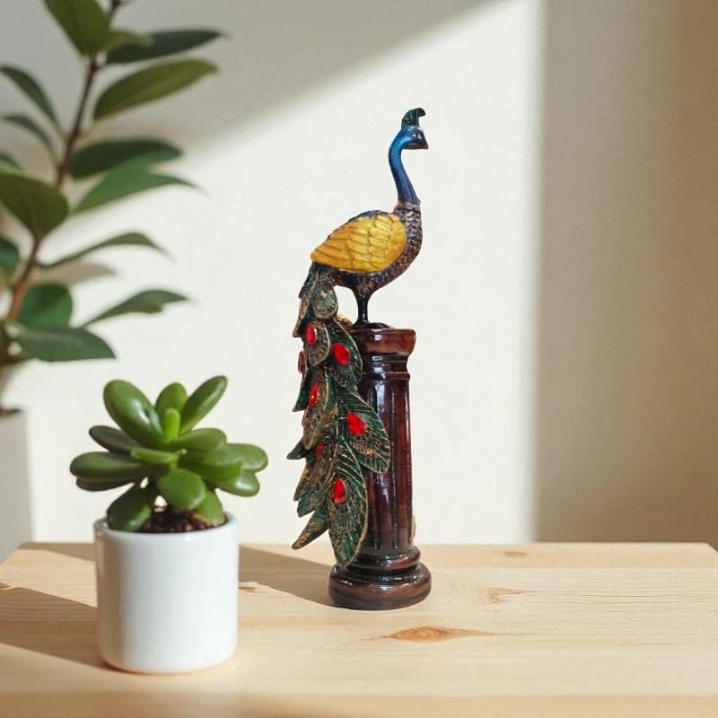 Decorative peacock statue on a wooden surface with a plant in the background