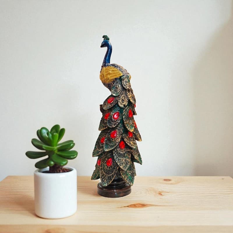 Decorative peacock figurine on a wooden surface with a plant in the background