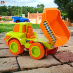 Toy dump truck with orange bed and green body on a brick surface