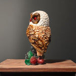 Side view of owl statue with textured wings and glossy red eyes