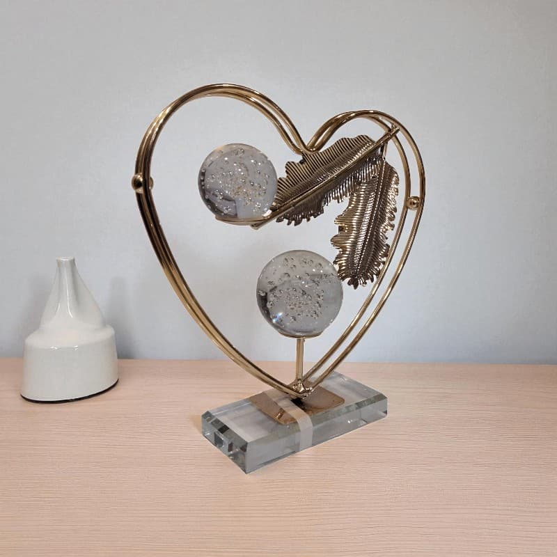 Decorative heart-shaped metal sculpture with glass spheres on a wooden surface.