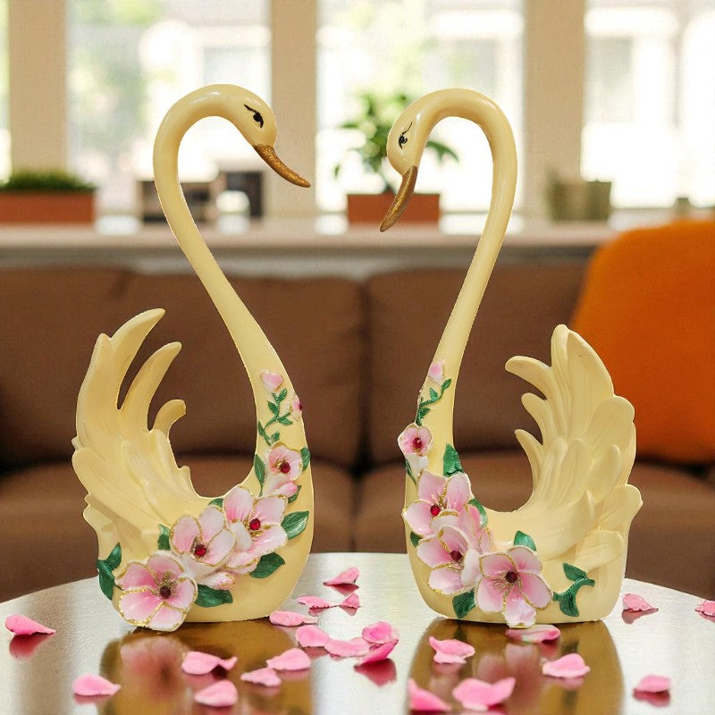 Decorative swan figurines with floral designs on a table with pink flower petals.