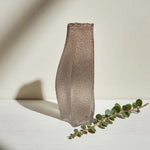 Textured vase on a light surface with a branch of eucalyptus leaves.