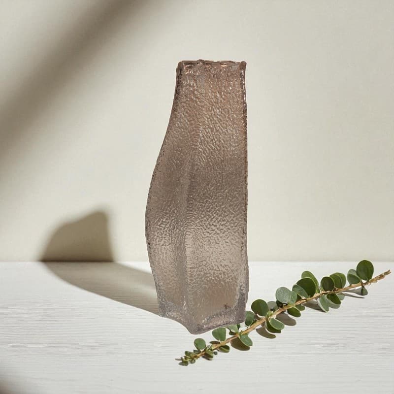 Textured vase on a light surface with a branch of eucalyptus leaves.