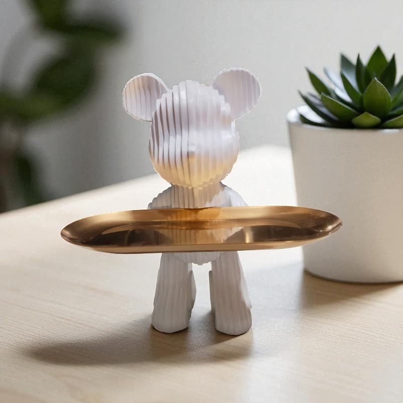 Decorative object shaped like a bear with a gold tray on a wooden surface with a plant in the background.