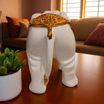 Decorative white elephant with gold accents on a wooden floor, next to a potted plant.