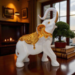 Decorative white and gold elephant statue on a table with a warm interior setting.