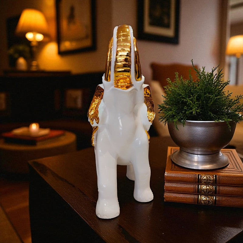 Decorative white and gold elephant figurine on a table with books and a plant in the background.