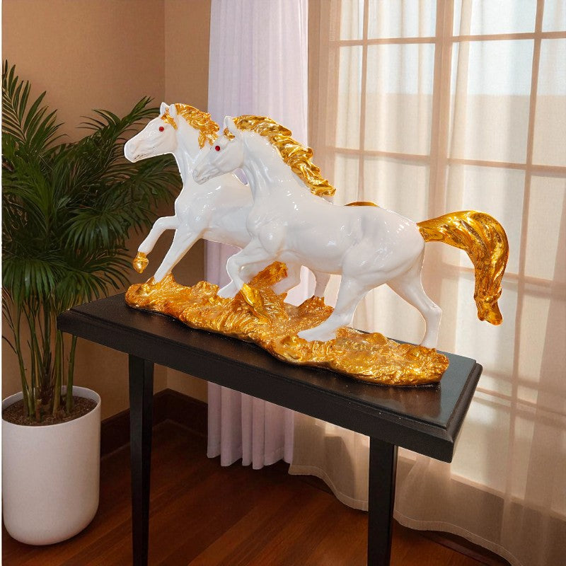 Decorative sculpture of two white horses with gold accents on a black platform in a room setting.