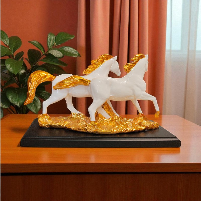 Decorative sculpture of two white horses with gold accents on a black base, placed on a wooden surface.