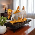 Decorative sculpture of two white horses with gold accents on a black base in a room setting.