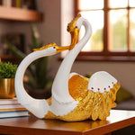 Decorative sculpture of two swans with gold and white colors on a wooden surface.