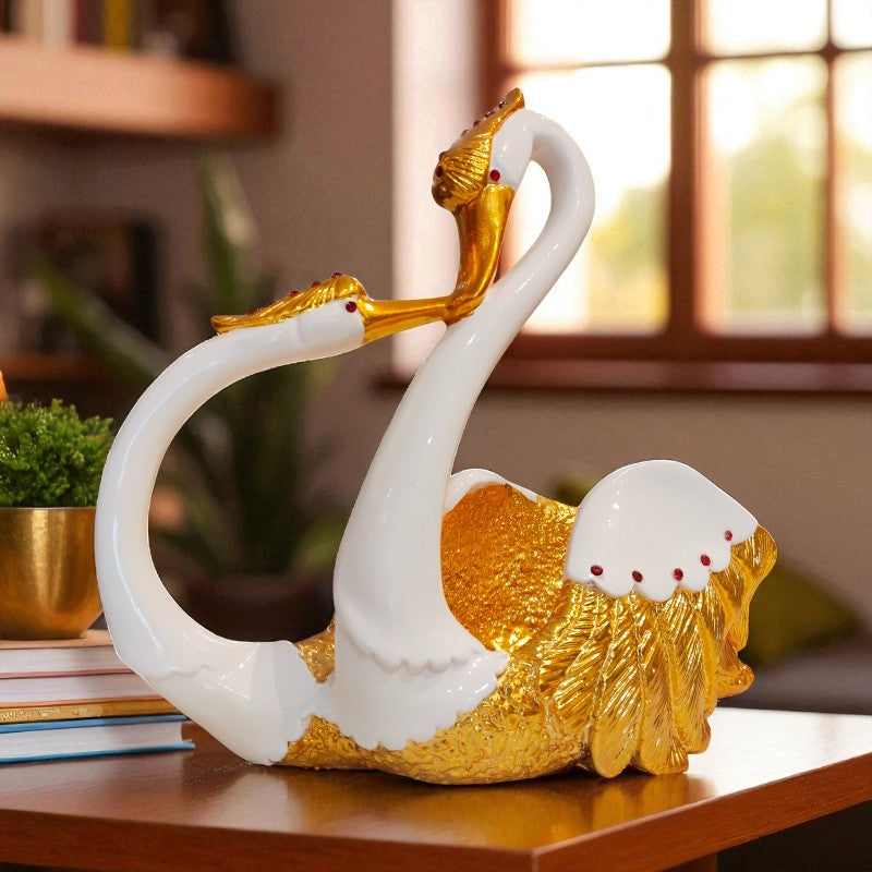 Decorative sculpture of two swans with gold and white colors on a wooden surface.